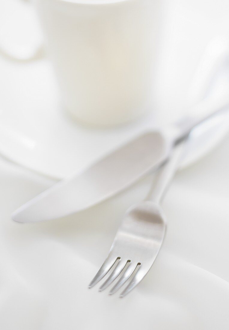 Messer und Gabel auf Kaffeetasse mit Untertasse