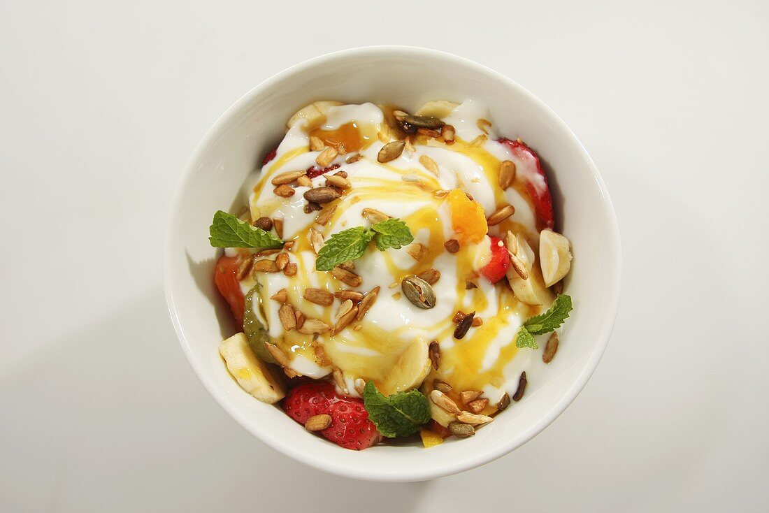 A fruit salad with yogurt and roasted pine nuts, seen from above