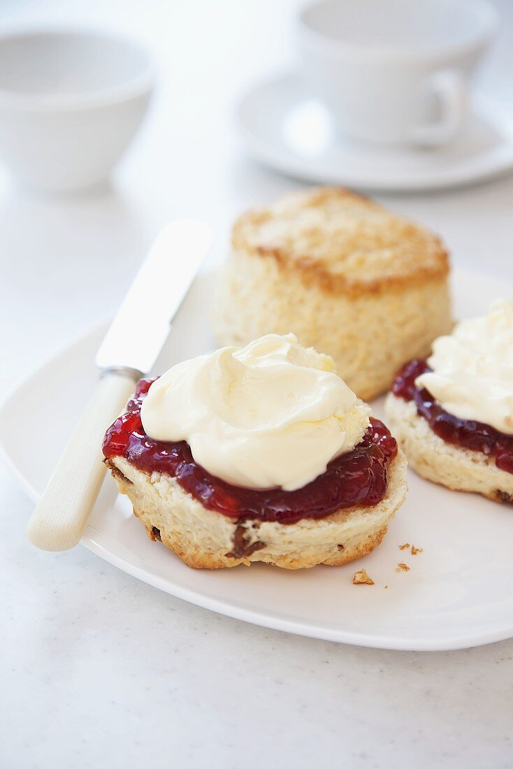 Scones with clotted cream and strawberry jam with tea cups in the background