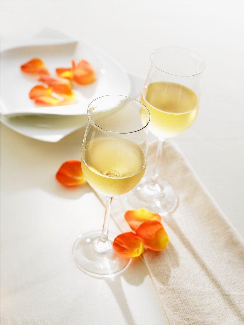 Two glasses of white wine on a table decorated with flower petals