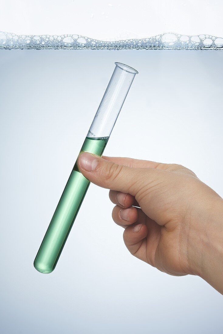 A hand holding a test tube of washing up liquid