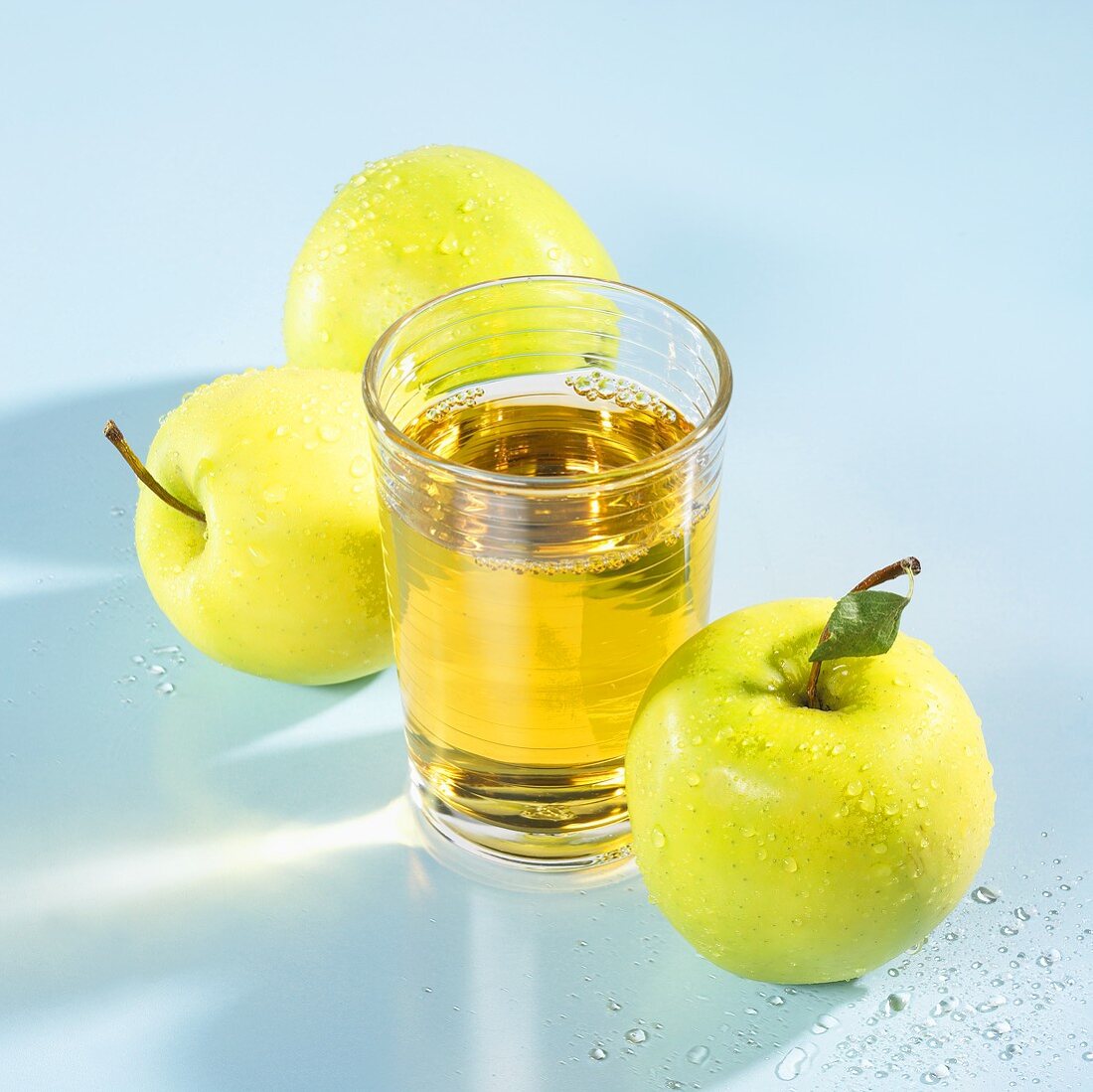 A glass of apple juice with apples beside it