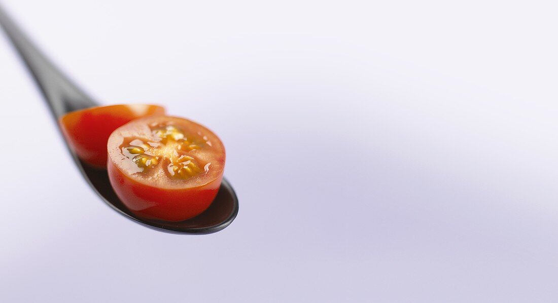 Cocktail tomato cut open on a black spoon
