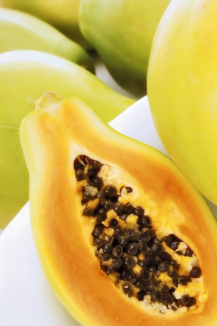 Papayahälfte neben ganzen Papayas