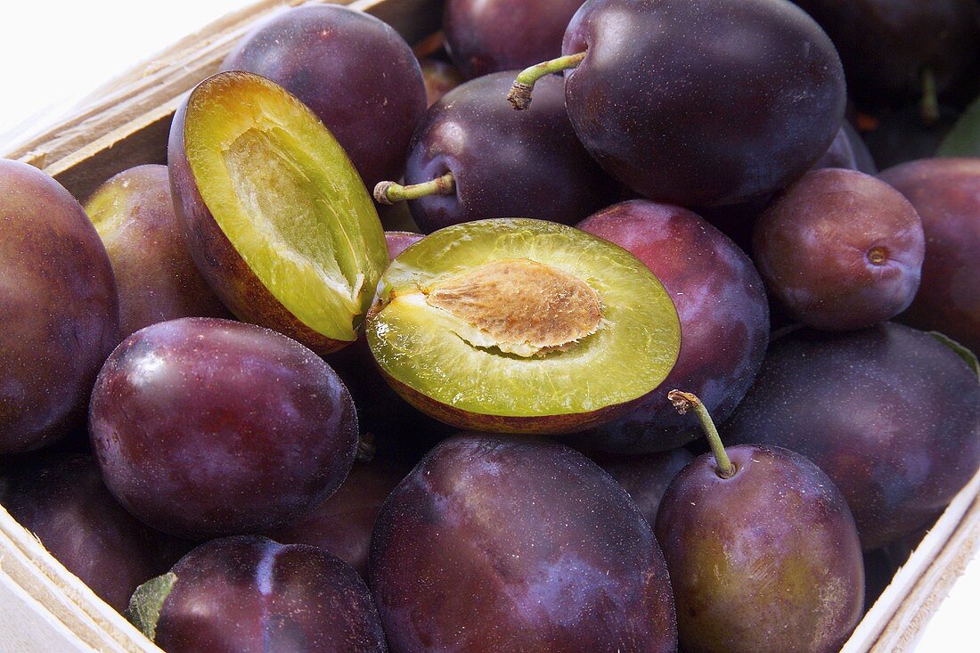 Plums in a cardboard punnet, one halved