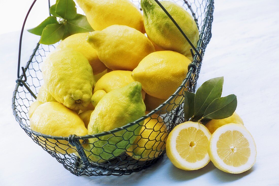 Bio-Zitronen in einem Drahtkorb, davor eine halbierte Zitrone