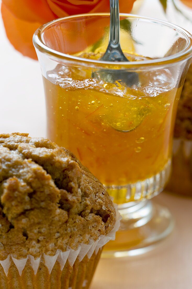 Orangengelee in einem Glas, davor ein Muffin