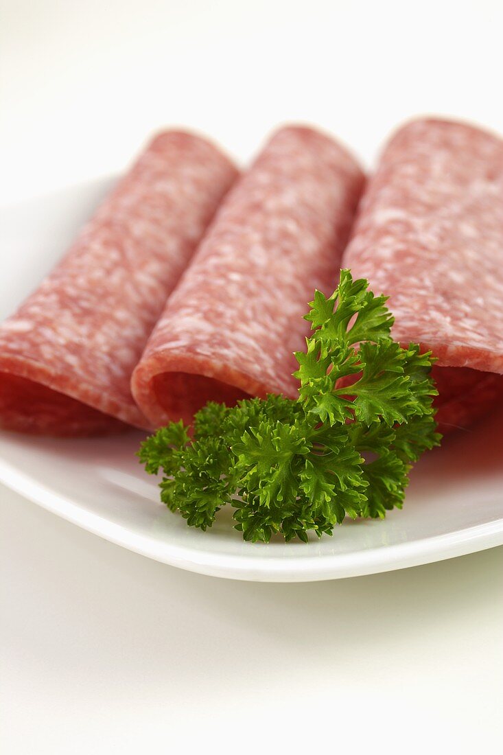 Three slices of salami with parsley on plate