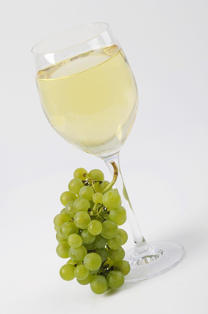 White wine grapes beside full white wine glass