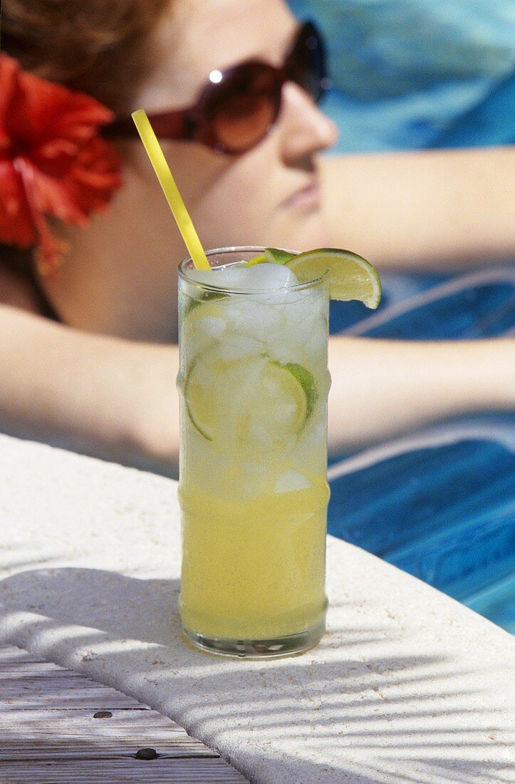Cocktail mit Limetten am Swimmingpool, Frau im Hintergrund