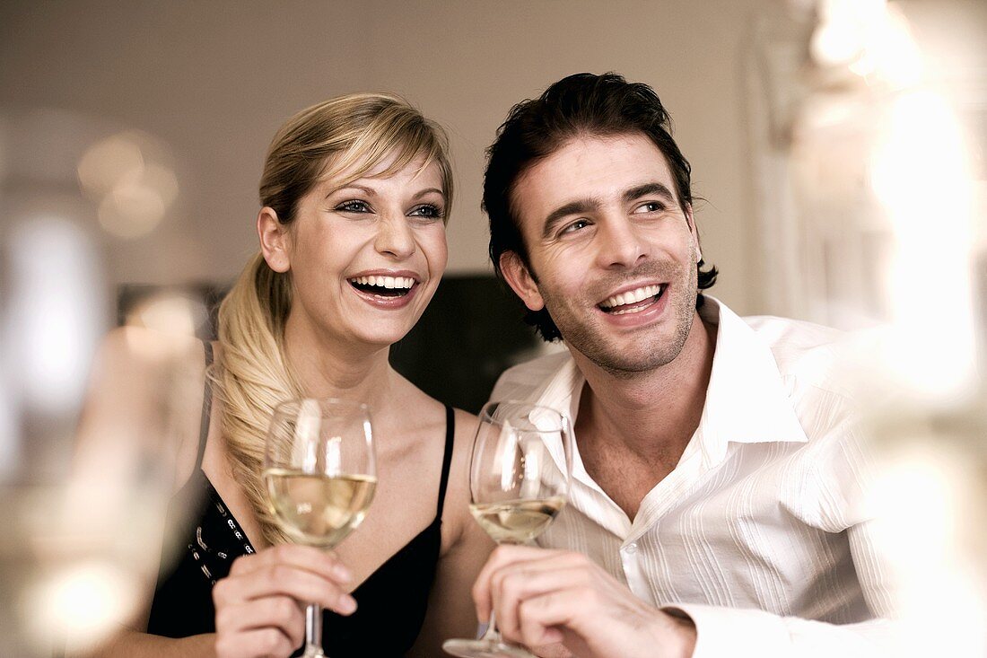 Laughing young couple with white wine glasses in their hands