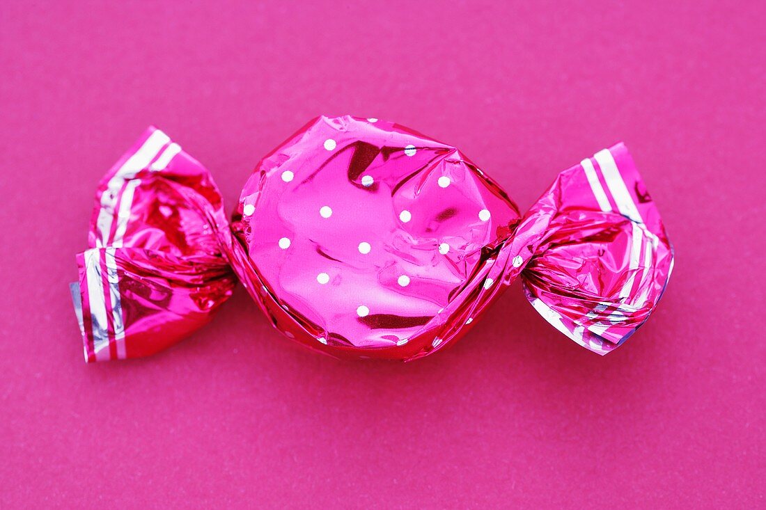 A sweet in a pink wrapper on a pink background