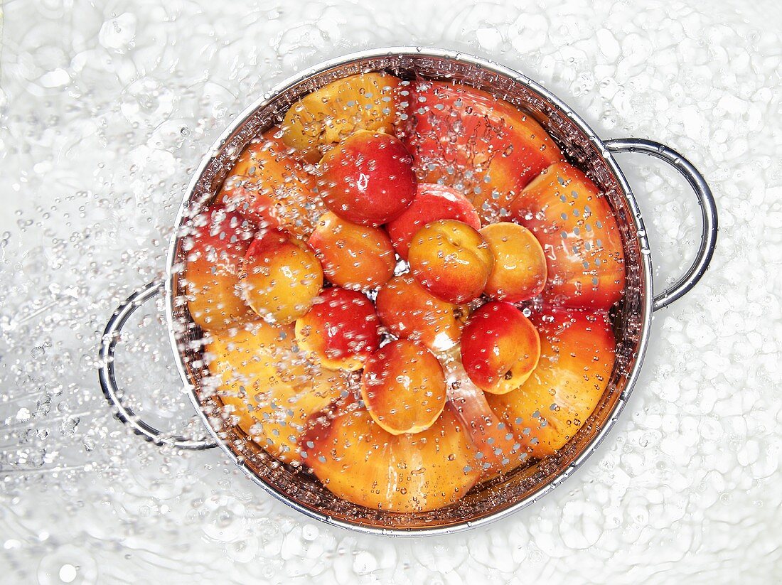 Apricots in a colander being sprayed with water