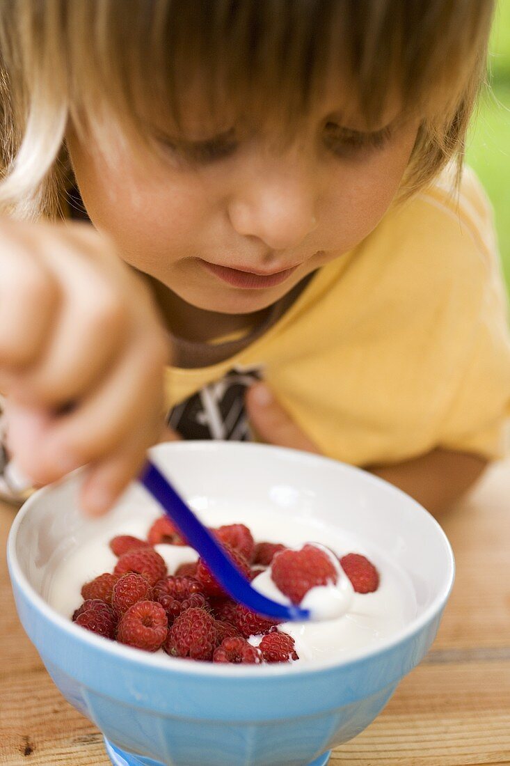Kleines Kind isst Joghurt mit frischen Himbeeren