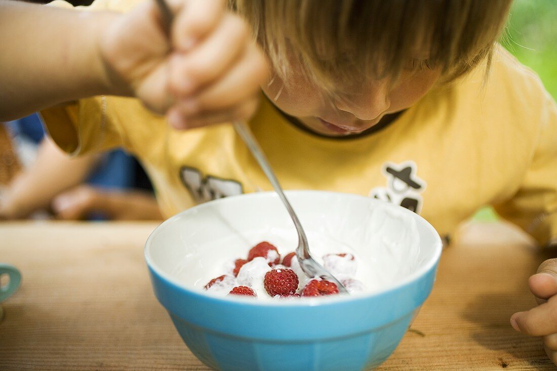 Kleines Kind isst Joghurt mit frischen Himbeeren