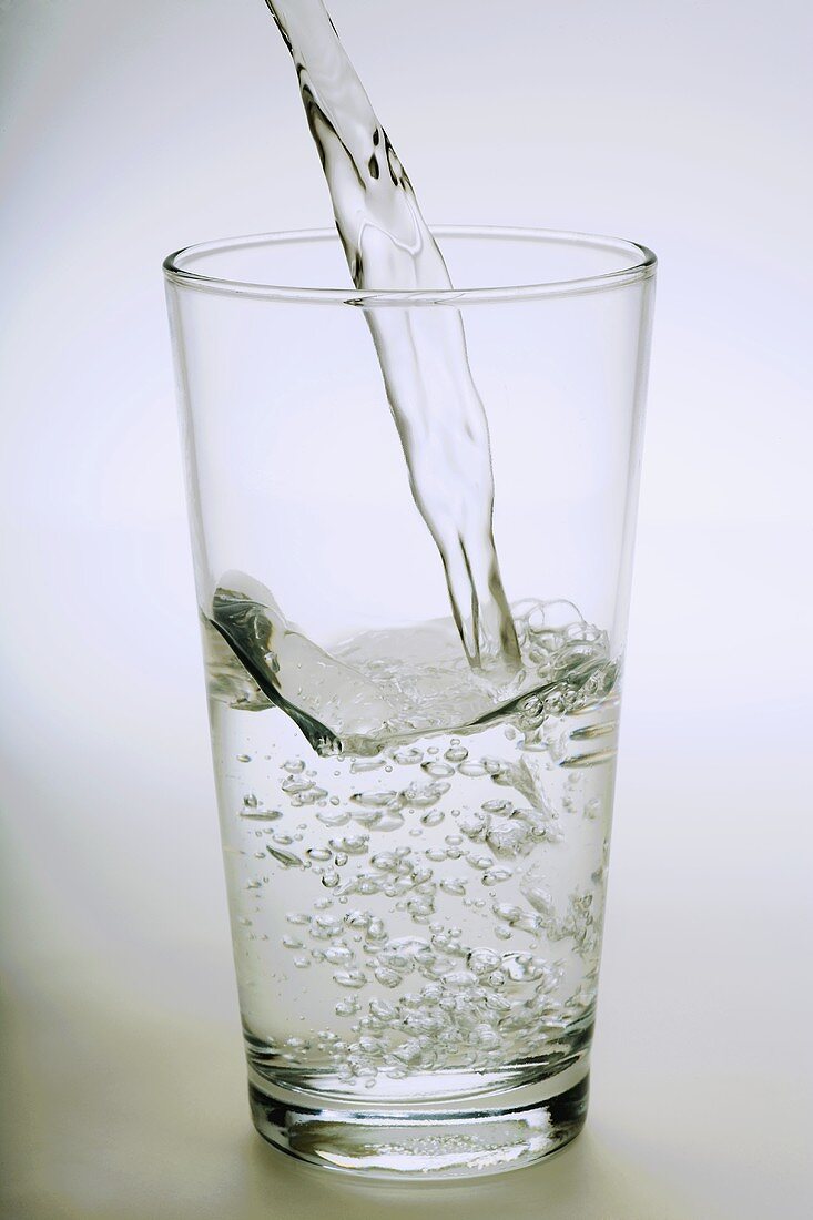 Ein Glas Mineralwasser eingiessen