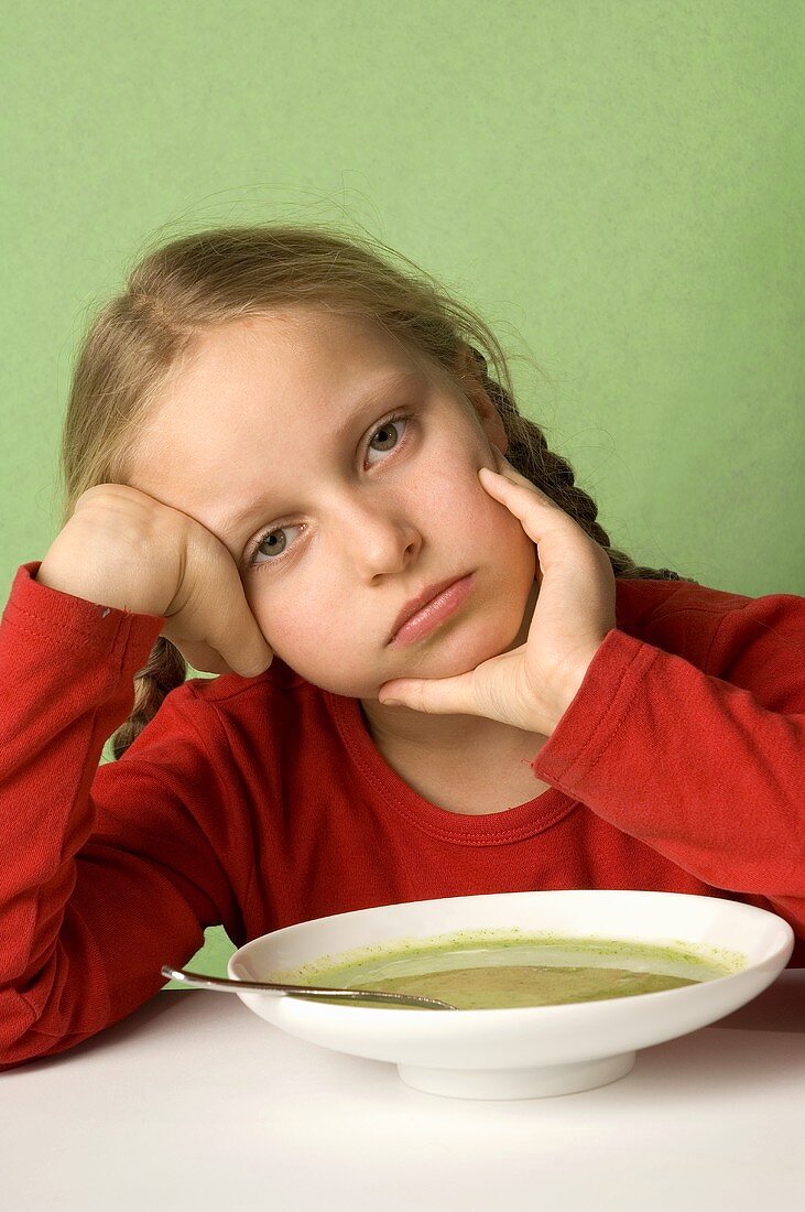 Mädchen sitzt lustlos vor Teller mit Gemüsesuppe