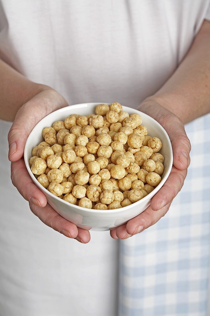 Hands holding a bowl of toasted rice breakfast cereal