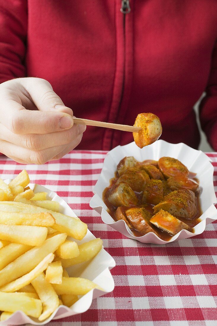 Person isst Currywurst mit Pommes Frites
