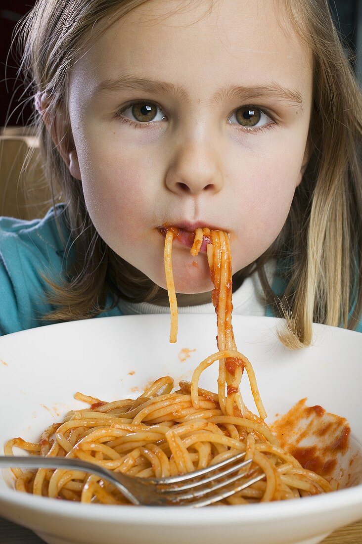 Small girl eating spaghetti with tomato sauce