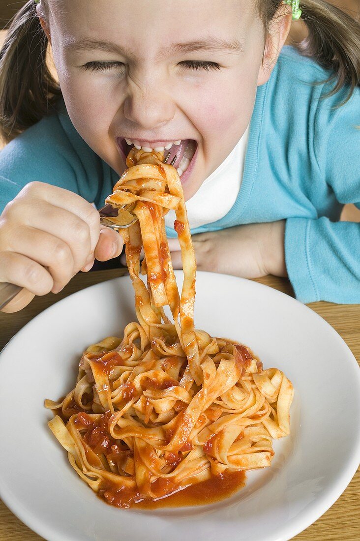 Small girl eating ribbon pasta with tomato sauce