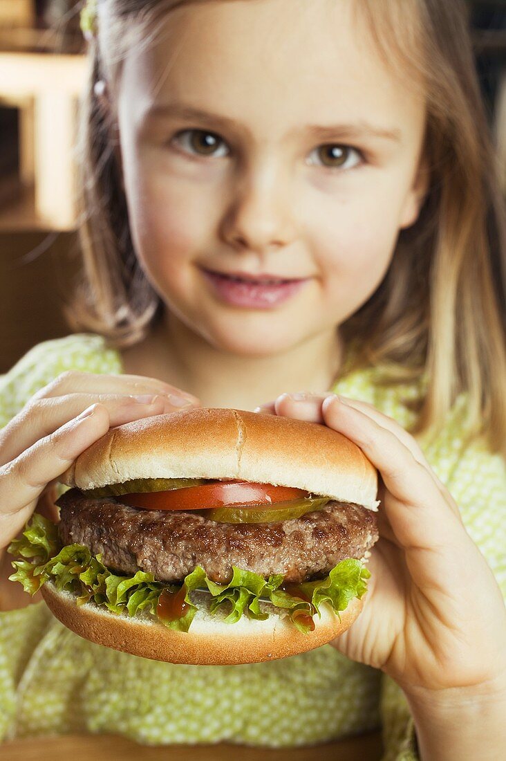 Kleines Mädchen hält einen Hamburger in den Händen