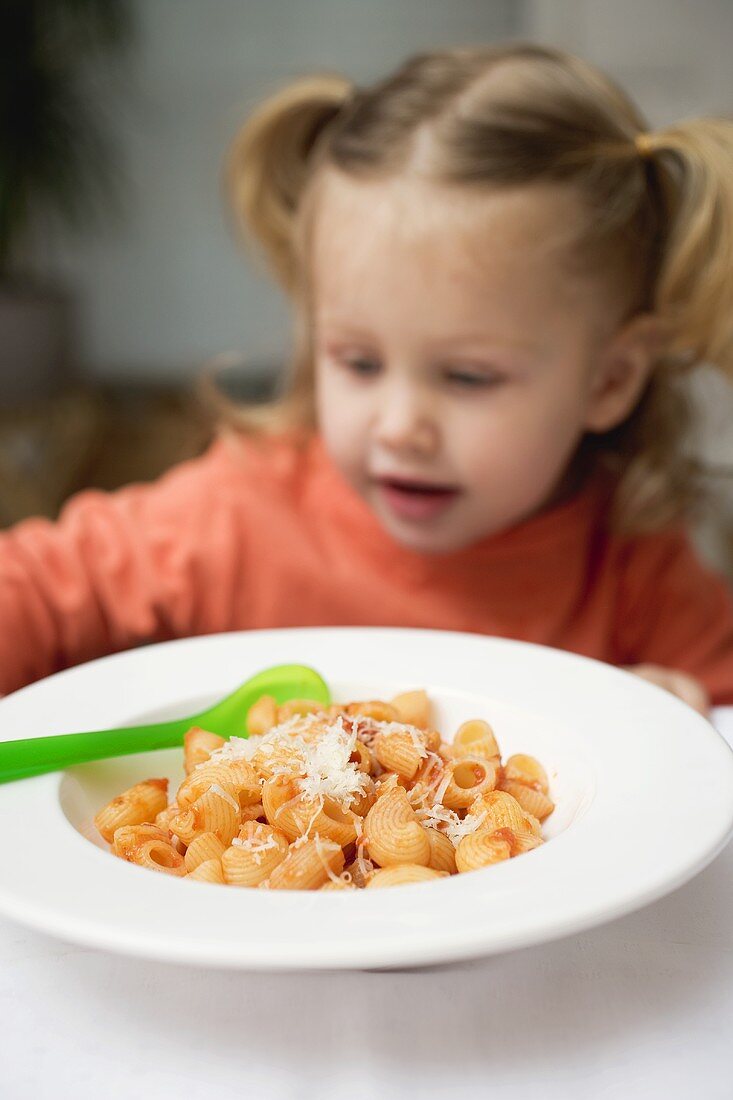 Kleines Mädchen sitzt vor Pasta mit Tomatensauce & Parmesan