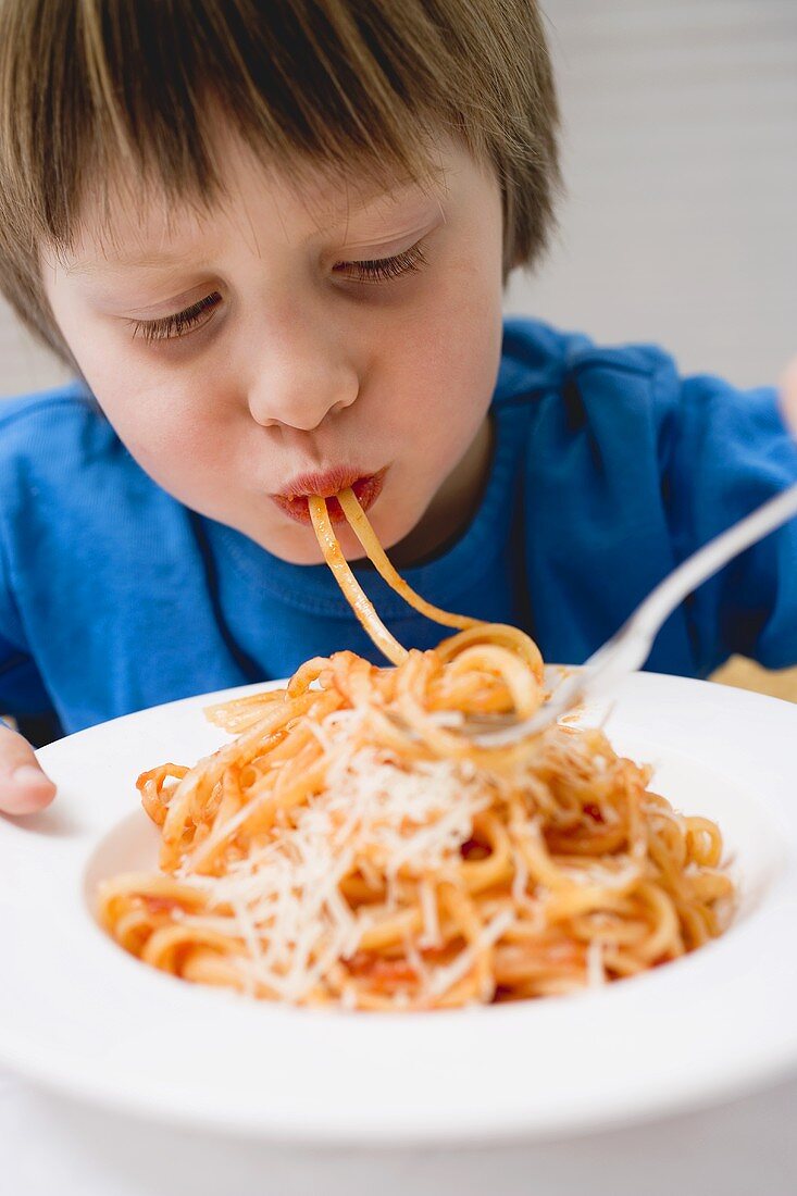 Small boy eating spaghetti with tomato sauce