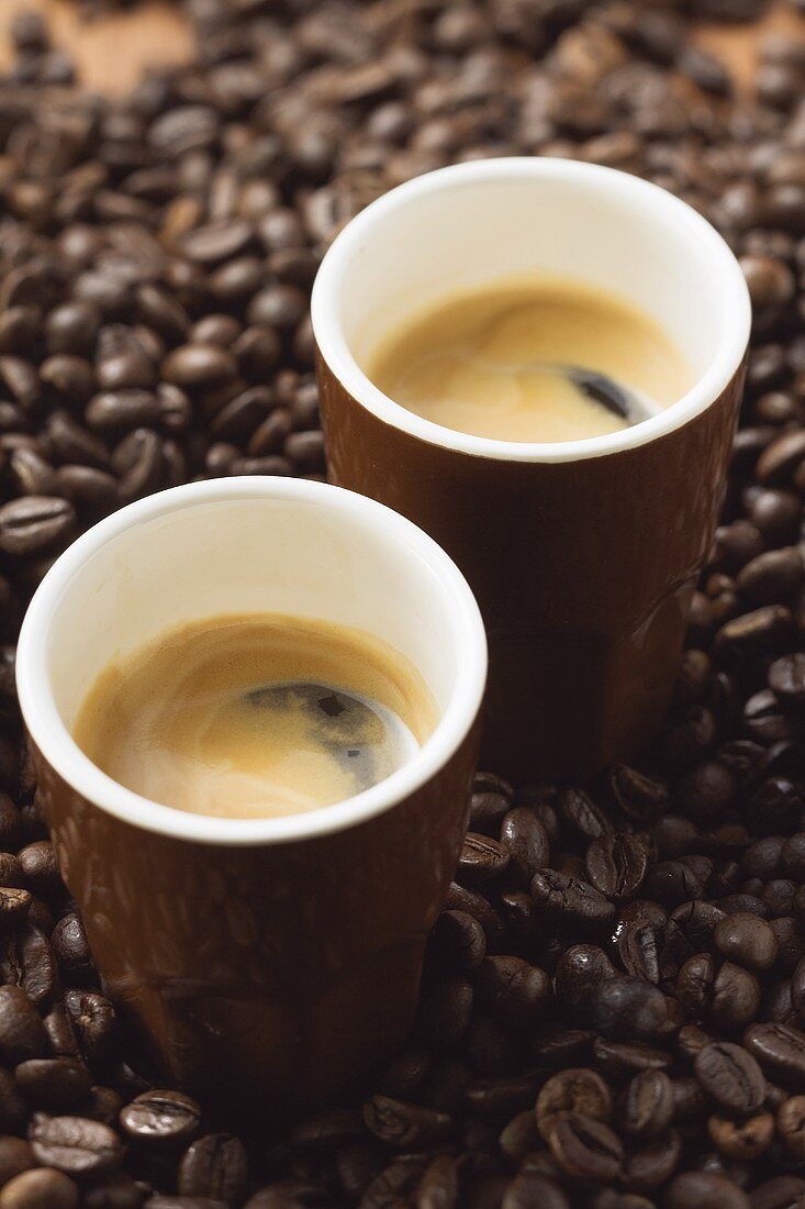 Two espressos standing on coffee beans