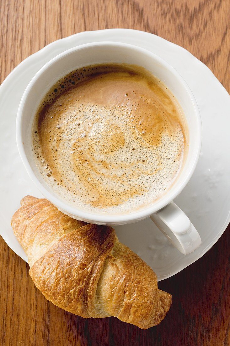 A cup of cappuccino with a croissant