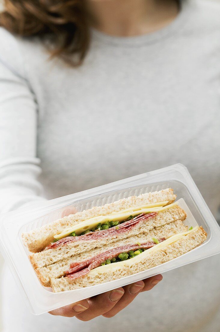 Frau hält zwei Salami-Käse-Sandwiches in der Verpackung