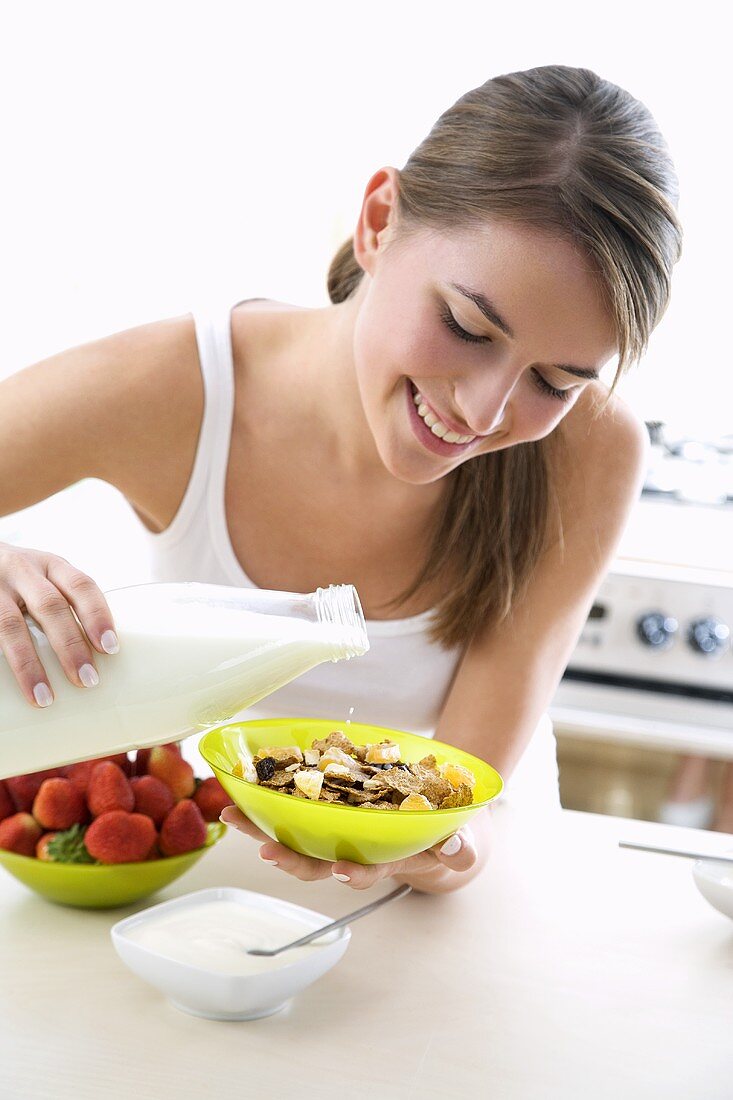 Junge Frau schüttet Milch in eine Schüssel Cornflakes