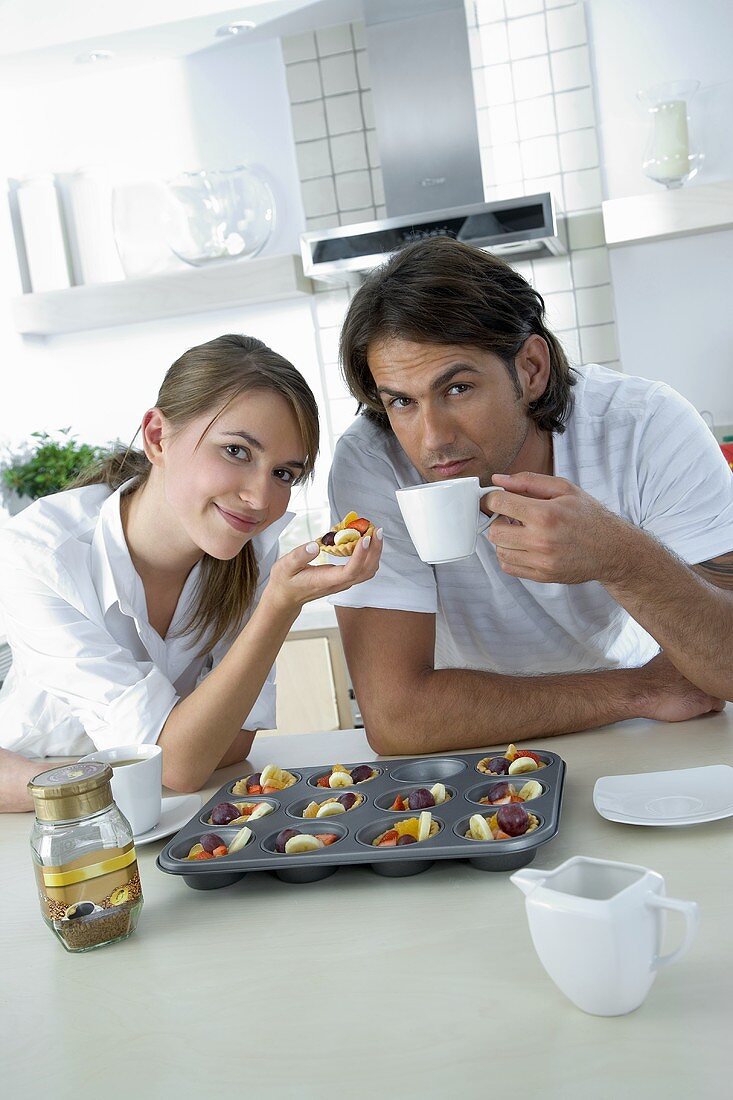 Young couple eating fresh fruit tarts and drinking coffee