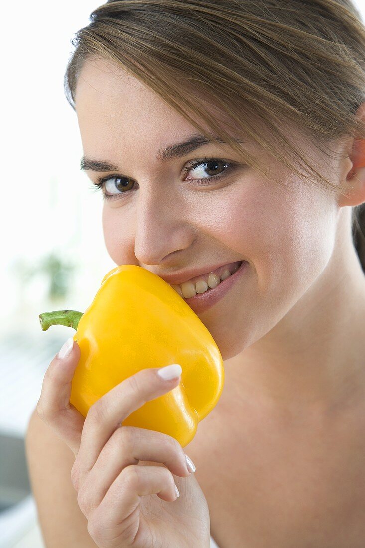 Junge Frau hält gelbe Paprikaschote vor den Mund