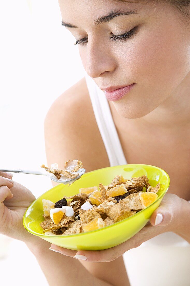 Junge Frau isst Cornflakes mit Früchten und Joghurt