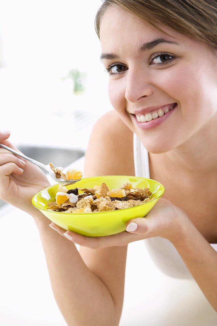 Junge Frau isst Cornflakes mit Früchten und Joghurt