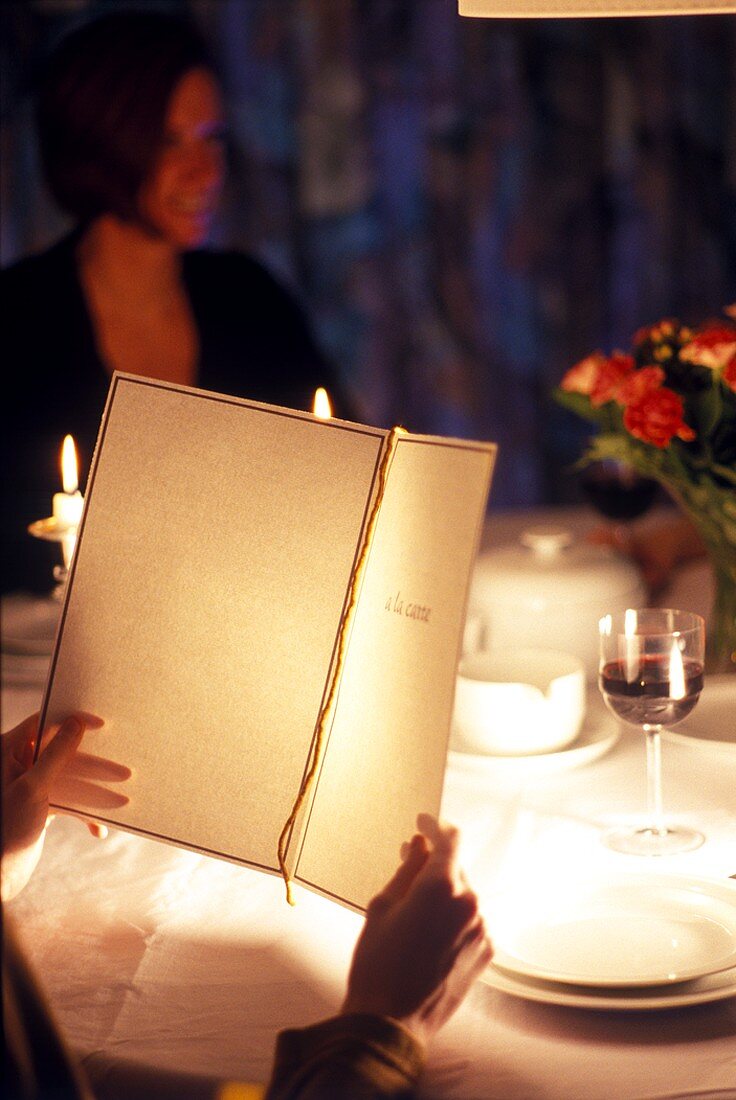 Guest reading menu in restaurant with woman in background