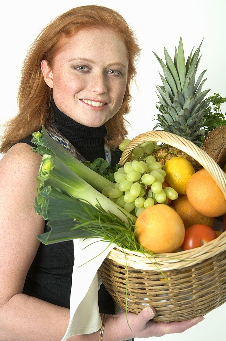 Junge Frau hält einen Obst und Gemüsekorb in den Händen