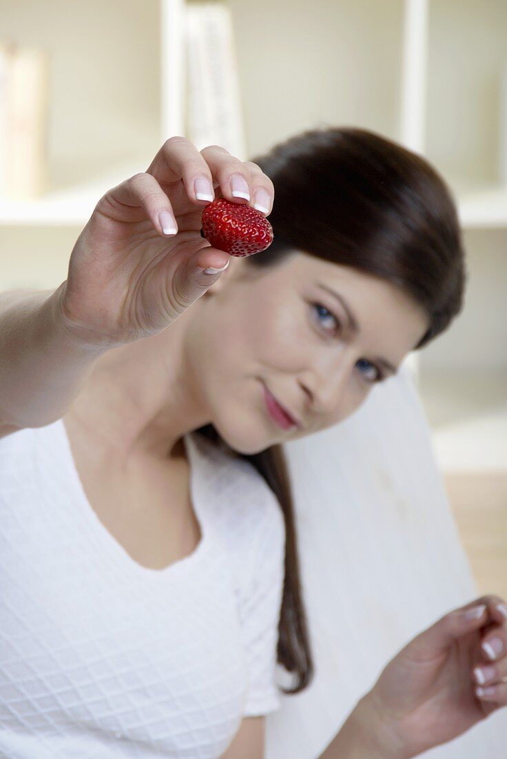 Woman holding a strawberry towards the camera