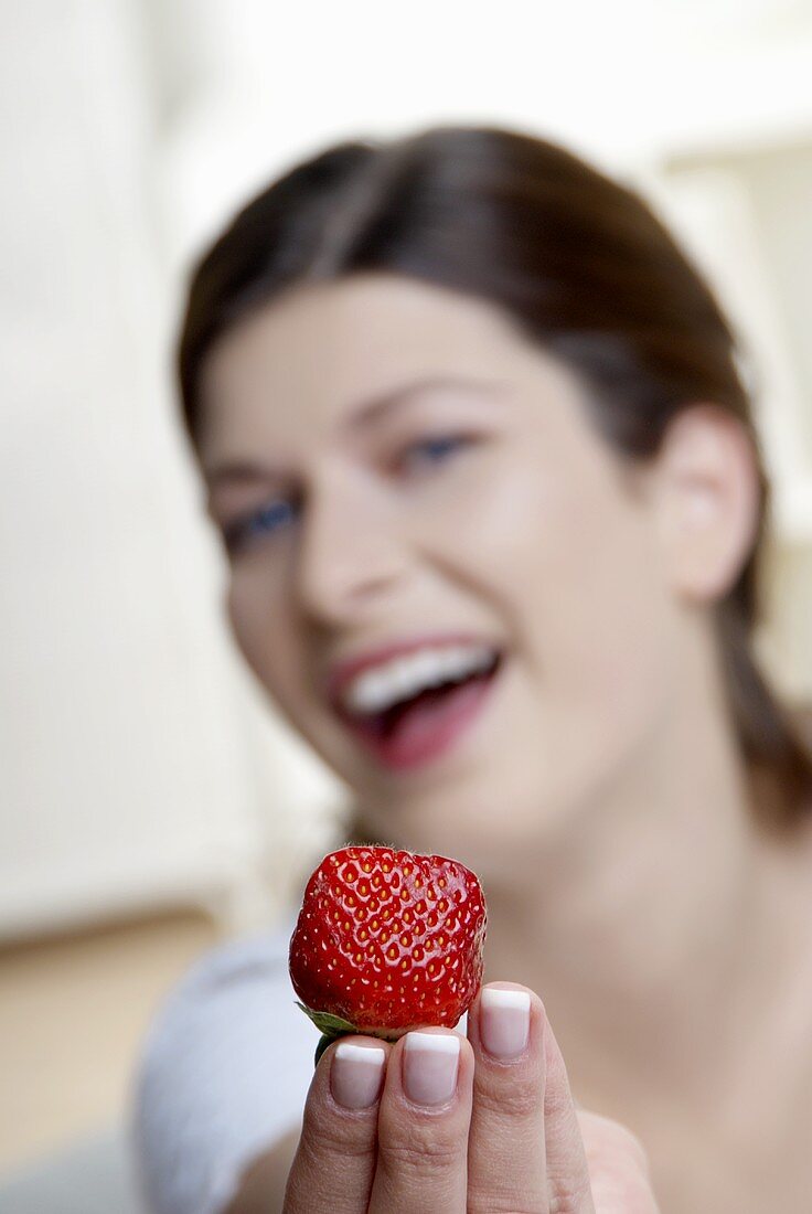 Frau hält eine Erdbeere mit ausgestreckter Hand
