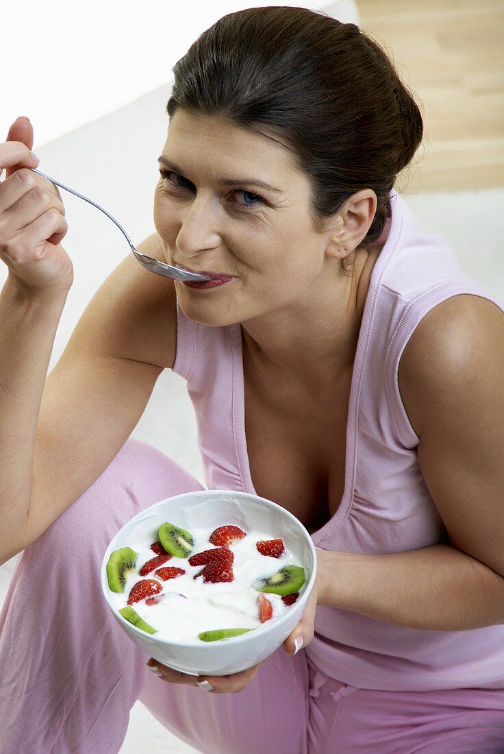 Frau isst Joghurt mit Kiwi und Erdbeeren