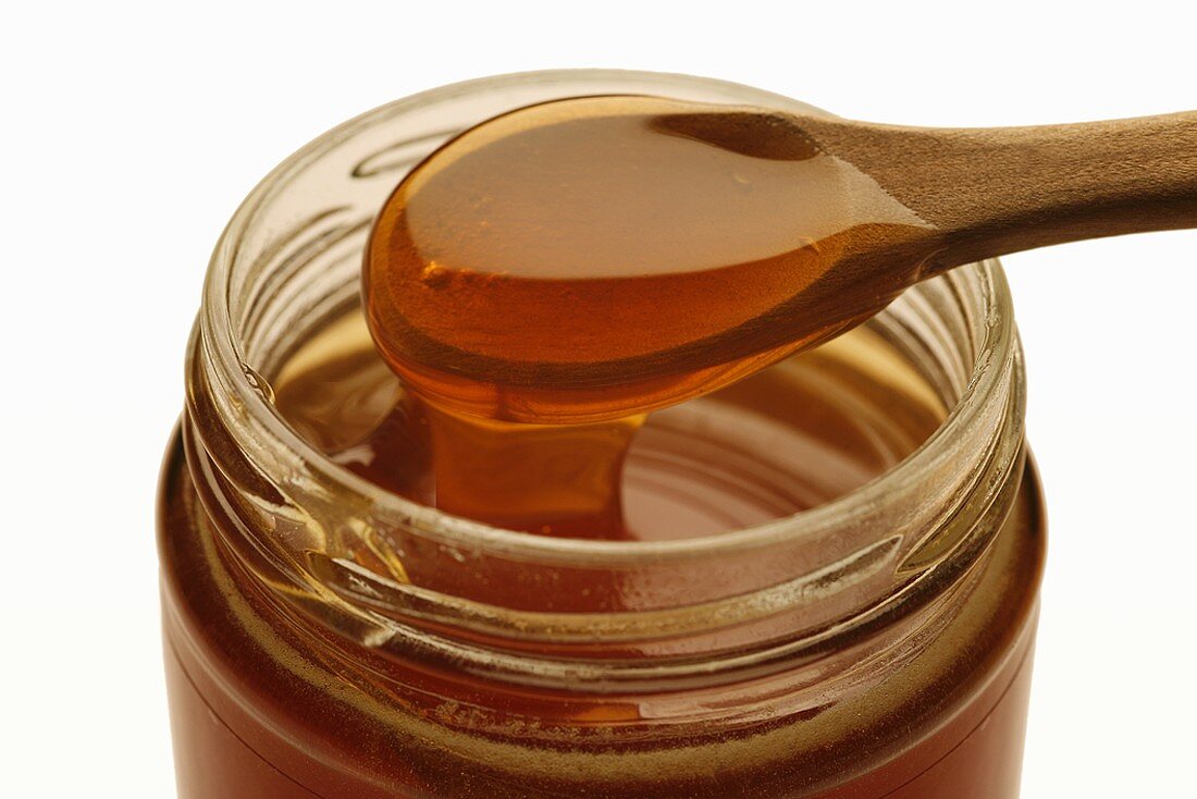 Manuka honey running into jar from wooden spoon