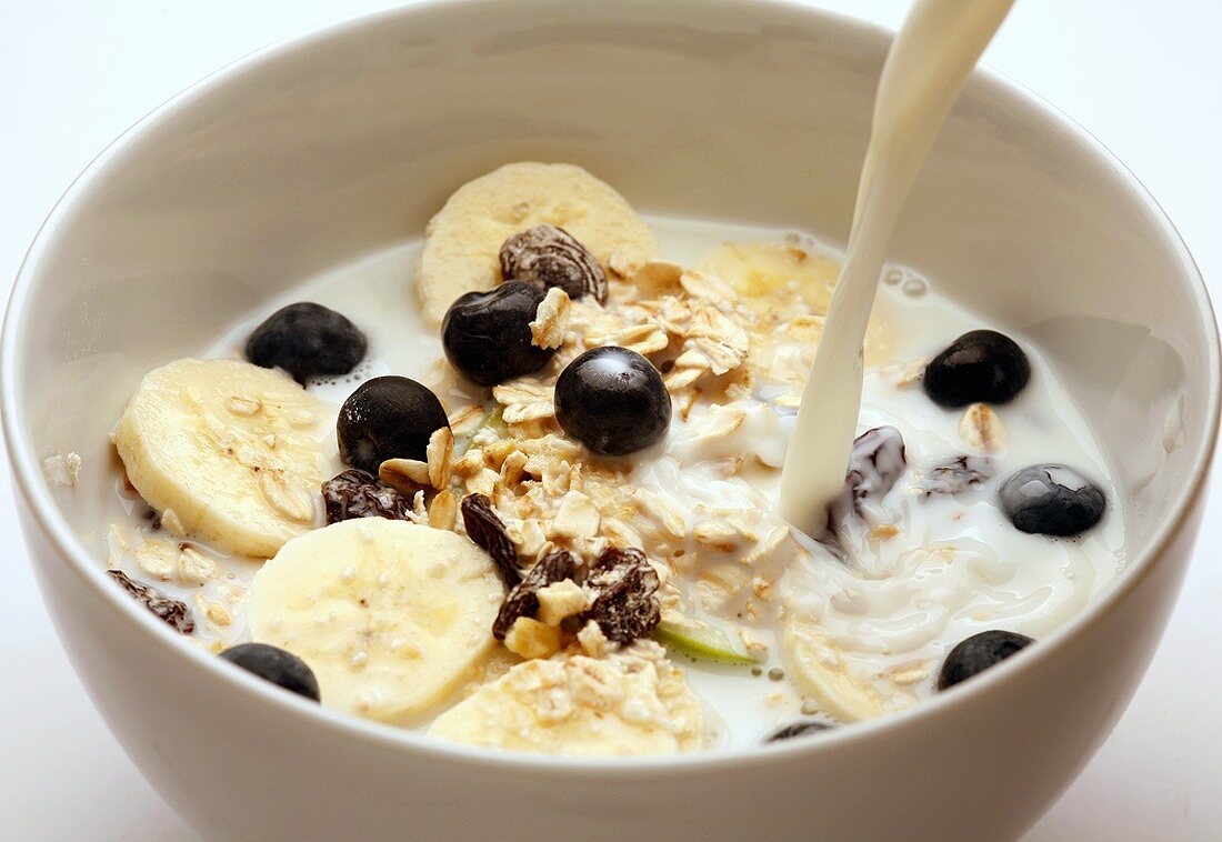 Pouring milk onto muesli with bananas and blueberries