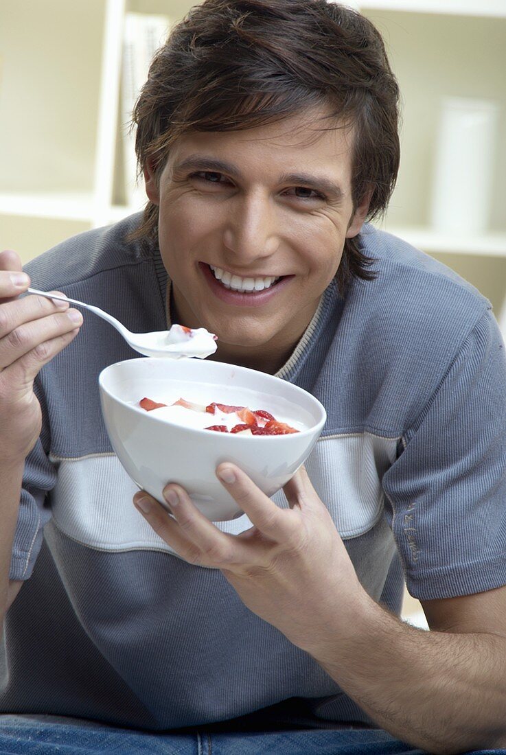 Young man eating quark with fresh strawberries
