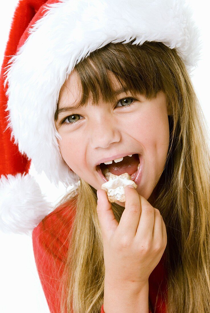 Girl in Father Christmas hat eating biscuit