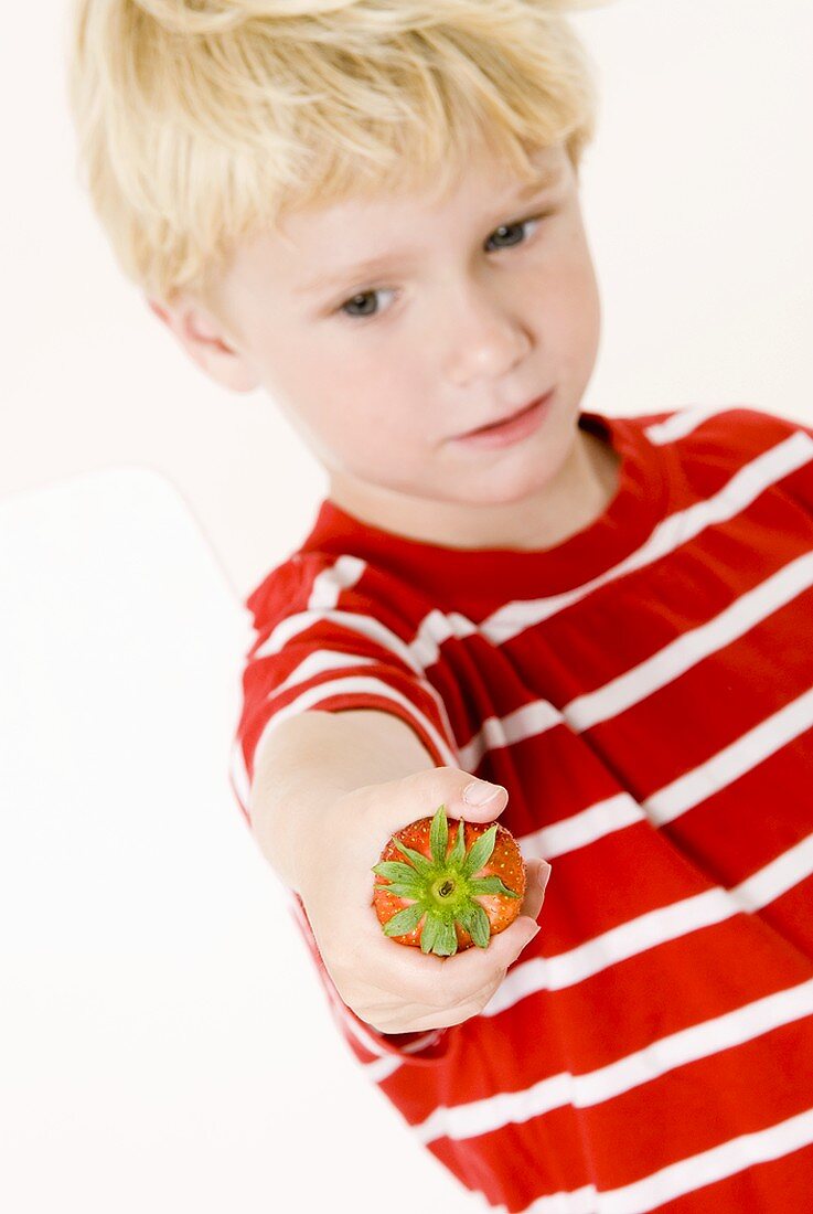 Blonder Junge mit einer Erdbeere in der Hand