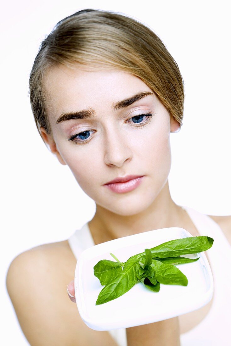 Young woman holding a plate of fresh basil leaves