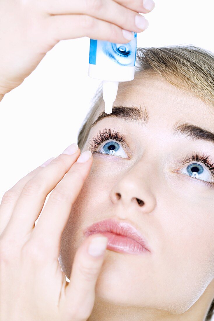Young woman putting drops into her eye