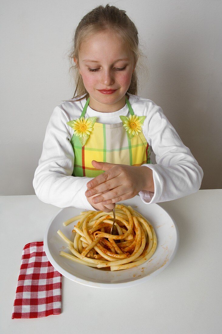 Girl twisting macaroni with tomato sauce around her fork