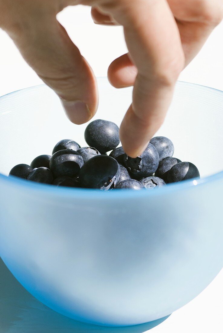 Hand reaching for blueberries in a small bowl